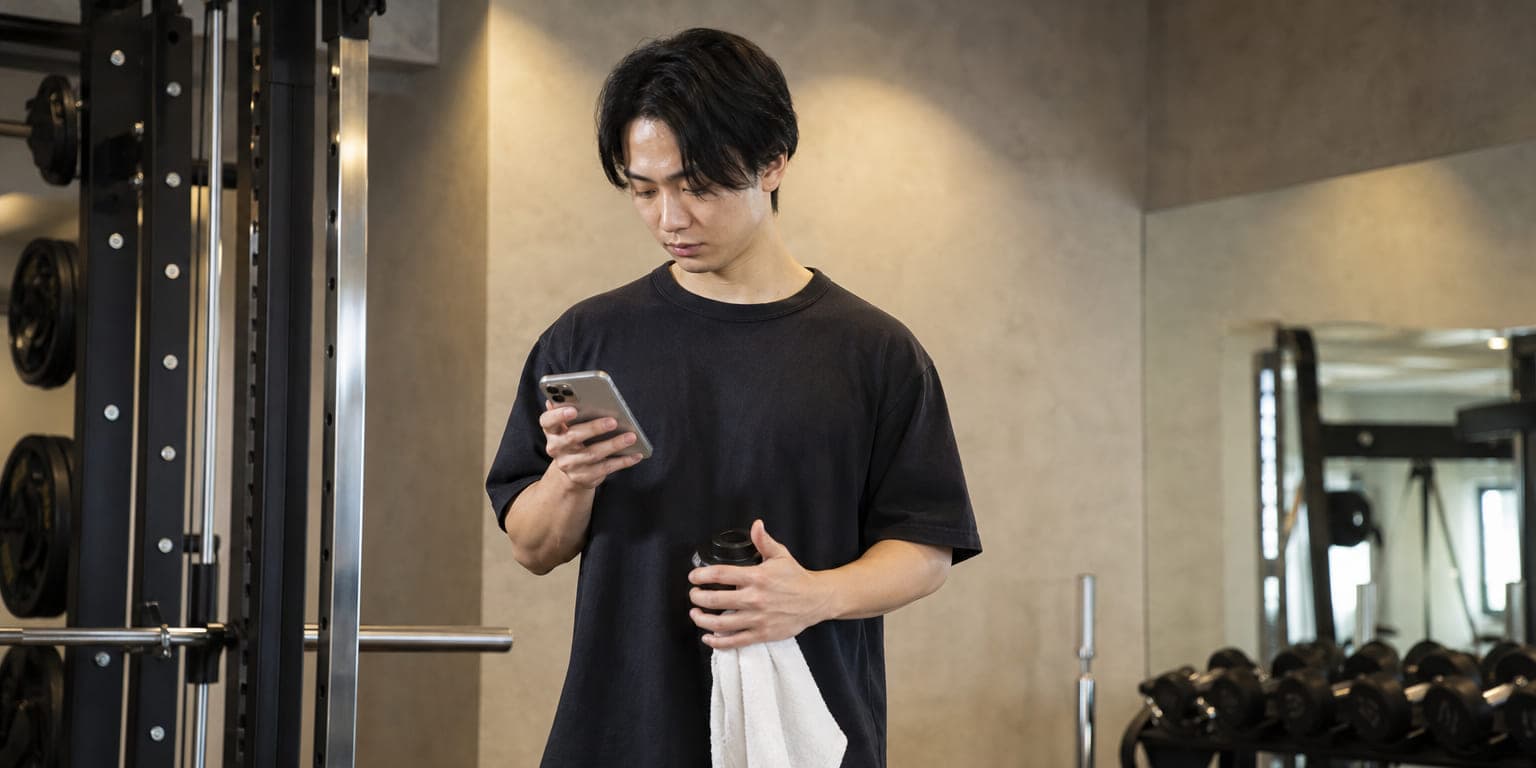 ジムでスマートフォンの予定を確認しながら自主トレーニングするクライアント