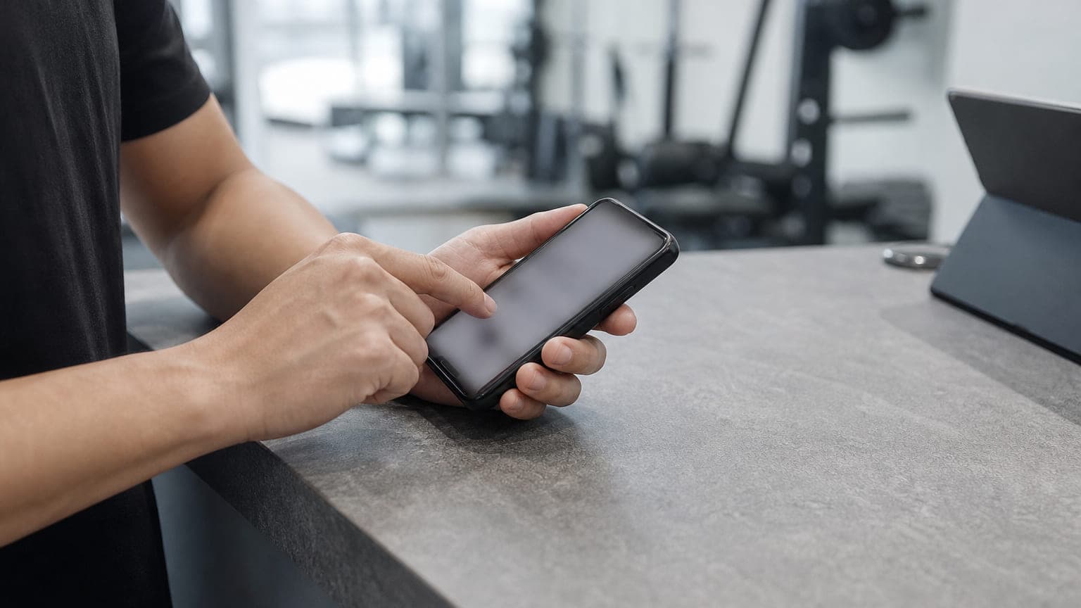 ジムのカウンターでスマートフォンからメッセージを送るトレーナーの手元